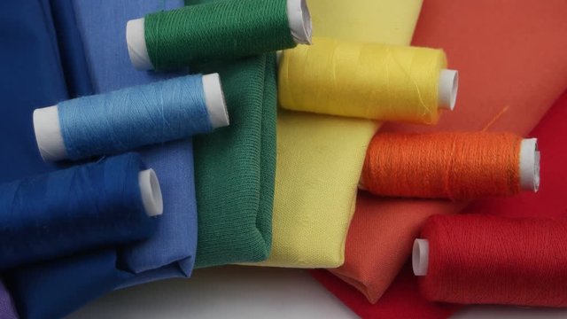 Composition of the set of colorful cotton fabric and spools of colorful thread are stacked in the spectrum of the colors of the rainbow on the white background