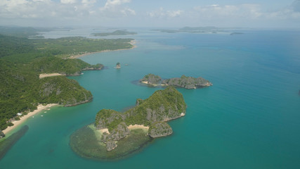 Naklejka premium Aerial view of Groups islands with sand beach and turquoise water in blue lagoon among coral reefs, Caramoan Islands, Philippines. Mountains covered with tropical forest.