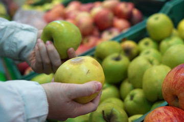 The buyer holding a fresh apple on the background of shelves with fruit.