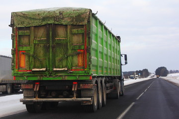 Heavy semi trailer truck with tented green open top container on winter road - transport, logistic