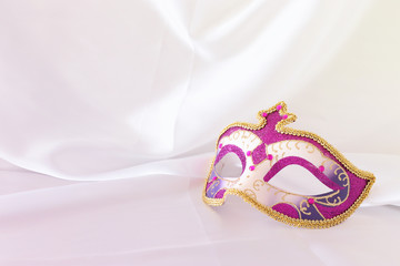Photo of elegant and delicate pink, purple and gold venetian mask over white silk background.