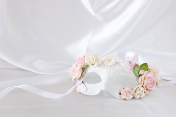 Photo of elegant and delicate white venetian mask with pink floral decorations over silk background.