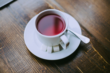 Red fruit tea with sugar cubes, cup of tea on the wooden background. Close up.