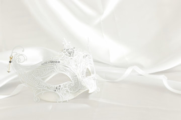Photo of elegant and delicate white lace venetian mask over silk background.