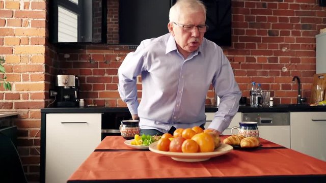 Mature man having backbone pain during breakfast at home.
