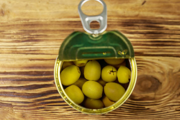 Open tin can of green olives on wooden table. Top view
