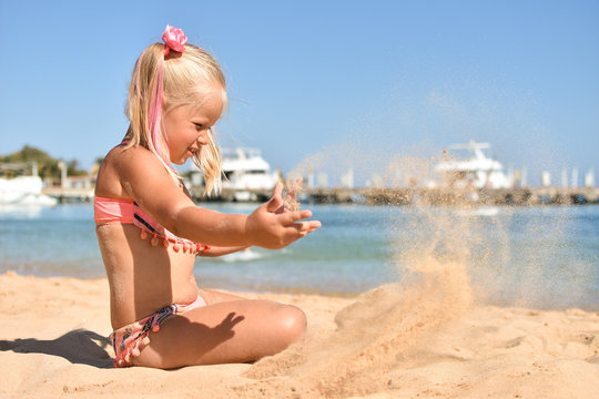 Girl playing with sand on the beach near the sea