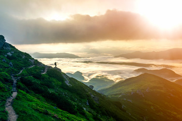Wide mountain panorama. Small silhouette of tourist with backpack on rocky mountain slope pointing...