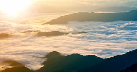 Fantastic view of mountain valley covered with low white puffy like snow clouds stretching to foggy...