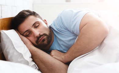 Fototapeta na wymiar Handsome young man sleeping in white bedding