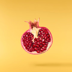 Flying in air fresh ripe pomegranate isolated on yellow background.