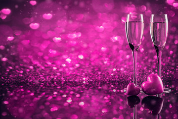 Two glasses of champagne with red heart shape bokeh on background.
