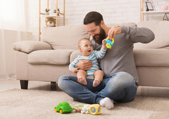 Happy father playing with his baby son with bright rattle