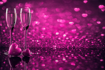 Two glasses of champagne with red heart shape bokeh on background.
