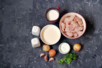 Ingredients for cooking homemade fish cakes: raw fish fillet, onion, garlic, milk, cornstarch, salt, pepper, breadcrumbs, parsley. Top view.