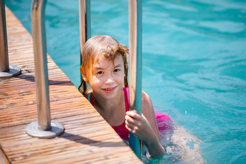 Little blonde girl in bright pink swimsuit having fun in the summer blue swimming pool
