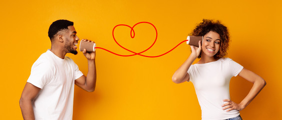 Young black couple with can phone on orange background