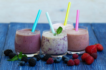 Raspberry, strawberry, blackberries, blueberry smoothie on blue wooden background. milkshake with fresh berries. healthy fruit smoothie with ingredients. well being and weight loos concept