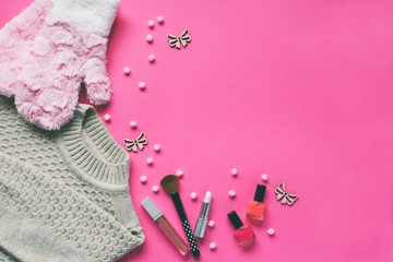 Knitted sweater, warm mittens, nail polishes, lipstick on a pink background. Winter and autumn set of warm, comfortable clothes and makeup cosmetics. Copy space. Top view