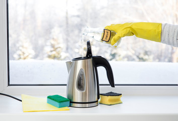 Woman pouring natural destilled acid white vinegar in electric kettle to remove boil away the...