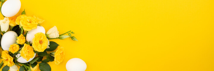 Frame made of flowers and eggs on a yellow background. Copy space.