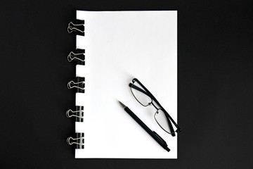 White sheets, pen, glasses and binder clip device for tying paper sheets together on black background close up