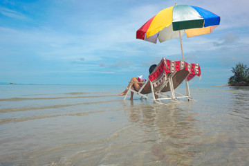 woman feel relax comfortable reading a book at middle of the sea under multicolor beach gamp umbrella at lowest tide, sitting on deck couch beach chair enjoy holidays and weekend vacation occasion