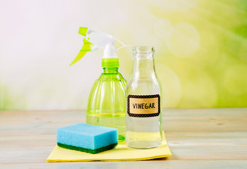 Chemical free home cleaner products concept. Using natural destilled white vinegar in spray bottle to remove stains. Tools on wooden table, green bokeh background, copy space.
