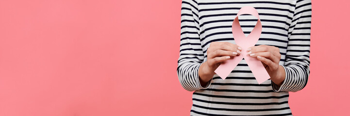 Midsection of a young woman holding pink breast cancer awareness ribbon isolated over living coral background. Healthcare, people, charity and medicine concept.