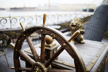 Wooden helm or sailing wheel with decorative ornaments on large ship floating upon river in urban...