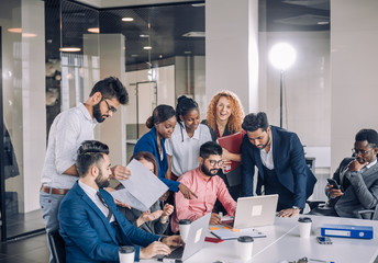 Woman showing coworkers something on laptop computer as they gather around a conference table