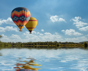 Colorful hot air balloon fly over the blue lake with reflection.
