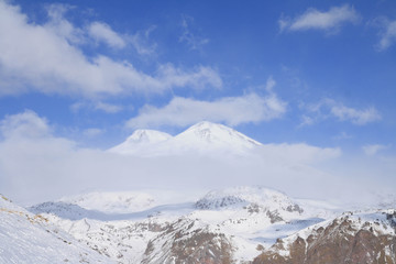 Fototapeta na wymiar Two-headed Mount Elbrus among the clouds. View from Mount Cheget, Baksan valley, Kabardino-Balkaria, North Caucasus, Russia