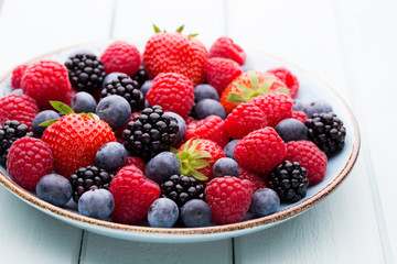Fresh berry salad on blue dishes. Vintage wooden background.