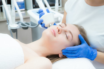 A young beautiful woman receives an electric facial massage on beauty equipment. Cosmetician in gloves. Modern cosmetology