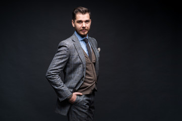 Fototapeta premium Pewnie elegancki przystojny młody człowiek stojący przed czarnym tle w studiu, ubrany w ładny garnitur.