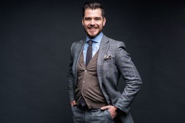 A confident elegant handsome young man standing in front of a black background in a studio wearing a nice suit.