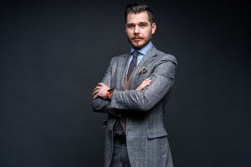 A confident elegant handsome young man standing in front of a black background in a studio wearing a nice suit.