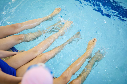 Close-up of little children sit on the edge of swimming pool and chat with their feet in the water