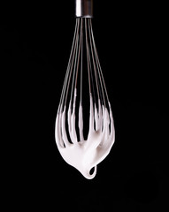 Metal whisk with whipped egg whites, isolated on black background. Clipping path.