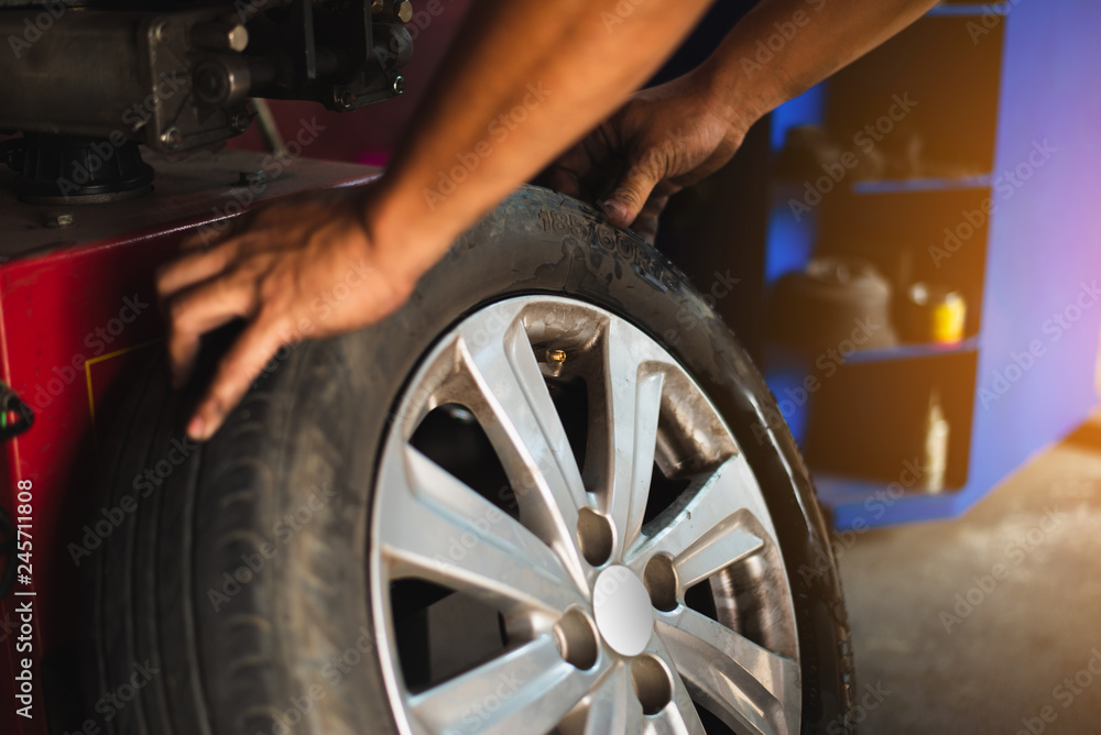 Poster technician balancing car wheel on balancer in workshop, man working in tire service workshop. mechan