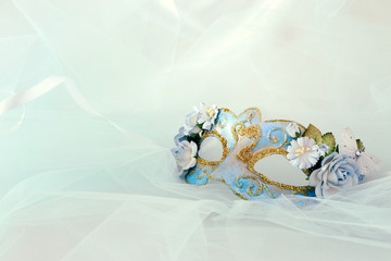 Photo of elegant and delicate blue venetian mask with floral decorations over mint chiffon background.