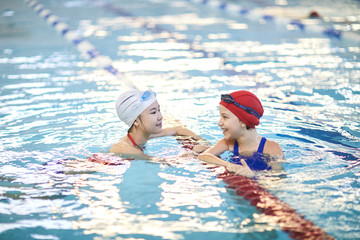 Two happy girls having fun in the water while they swimming in indoor pool