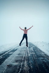 Fototapeta na wymiar Young girl looking like floating over a foggy endless winter road in white winter landscape. Back view of a person jumping. Harz Mountains National Park in Germany