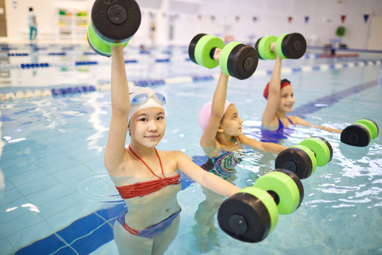 Group of little girls in swimsuit standing and training with dumbbells in swimming pool