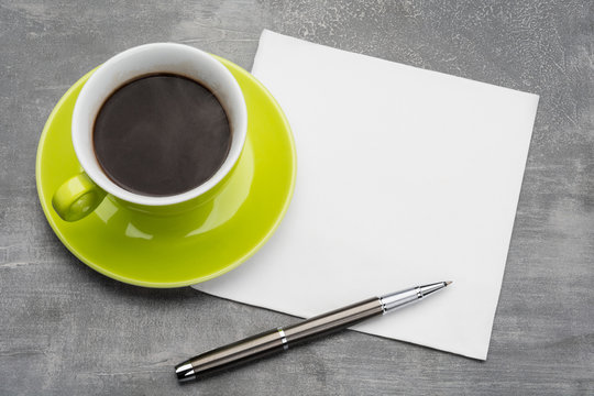 Green cup of coffee with  clean napkin and a metal ballpoint pen on grey background