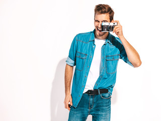 Portrait of handsome smiling man wearing summer hipster jeans clothes. Model male taking picture on old vintage photo camera. Isolated on white