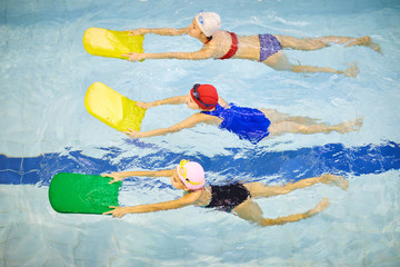 Group of little girls in swimwear swimming with kickboards in pool during swimming lesson - Powered by Adobe