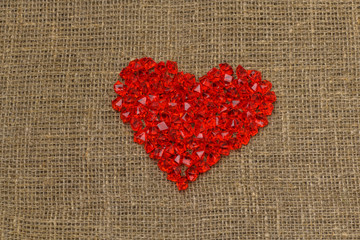 Valentine's day. A large red plastic glass heart of small crystals lies on a brown burlap (bag). Horizontal photography