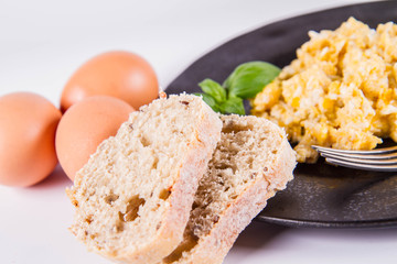 Scrambled eggs, some fresh eggs and wholemeal bread, and a fork, decorated with basil, on a white background 